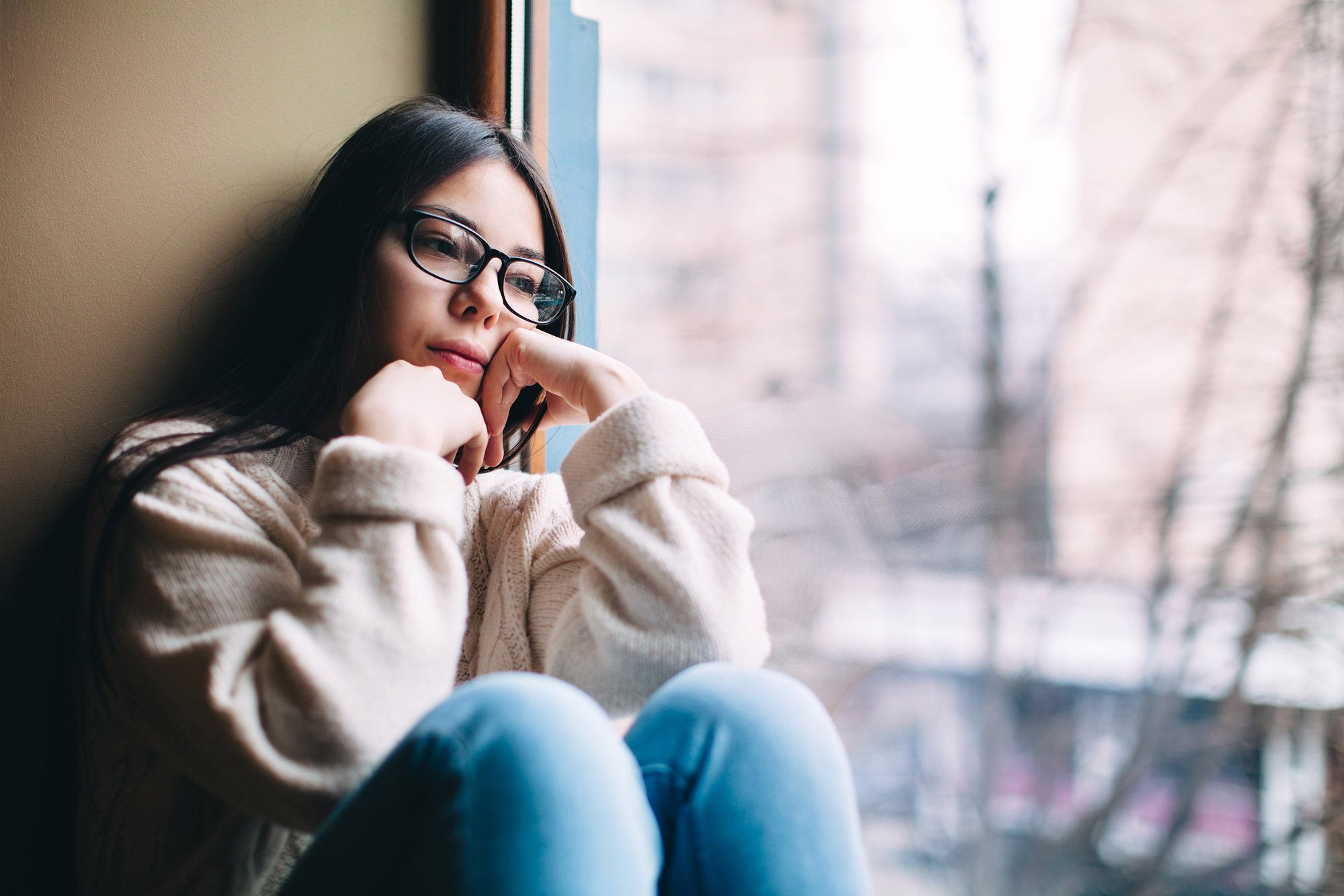 Sad teenage girl looking out the window on a cold autumn day