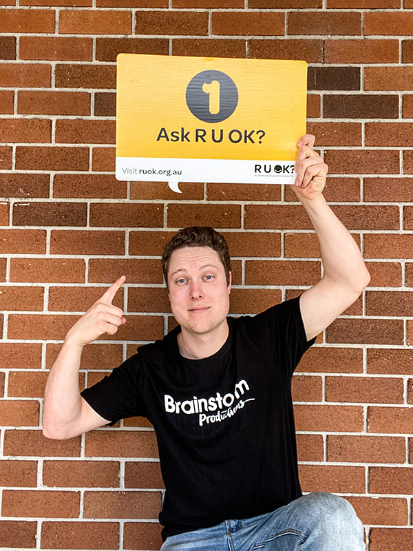 Brainstorm Productions actor Blake holding a sign that says 1. Ask R U OK?