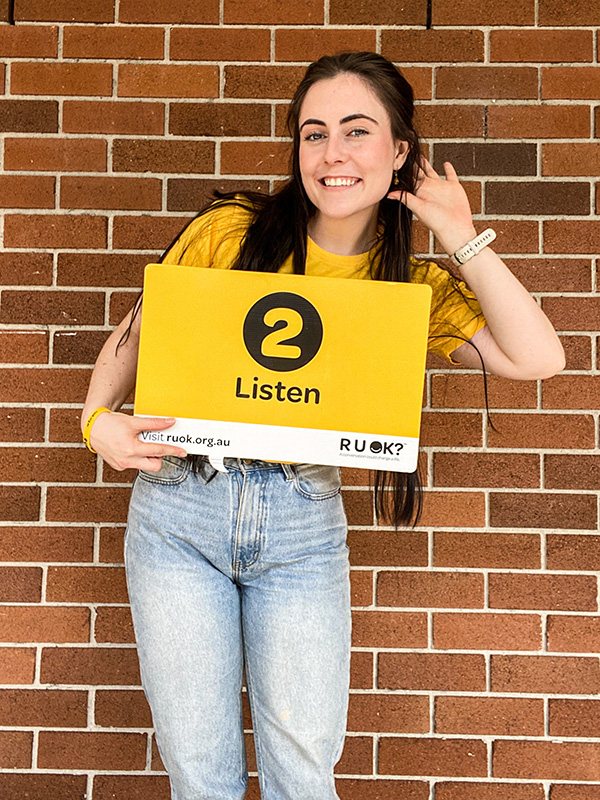 Brainstorm Productions actor Dani holding a sign that says 'Step 2: Listen'