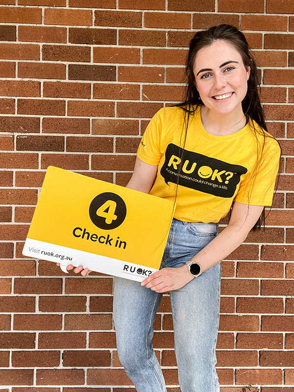 Brainstorm Productions actor Dani holding a sign that says 'Step 4: Check in'