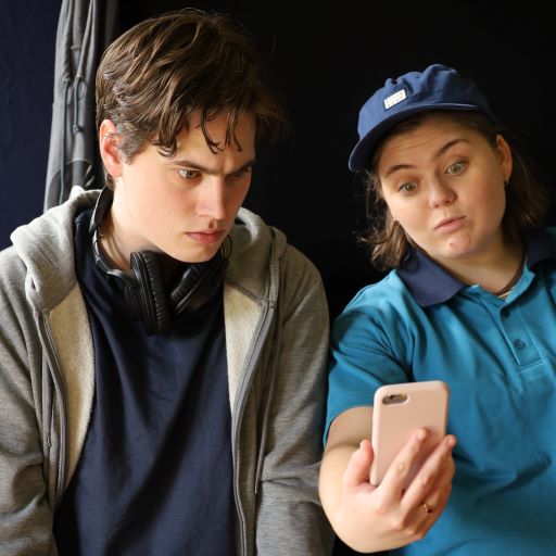 A still from the high school show Wired - two actors are looking at a phone, one looks shocked, the other looks amused