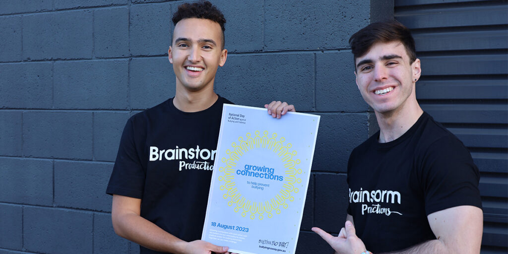 A promotional image for the National Day of Action Against Bullying and Violence 2023 (NDA) - two actors from Brainstorm Productions are holding an NDA poster that says 'Growing Connections'