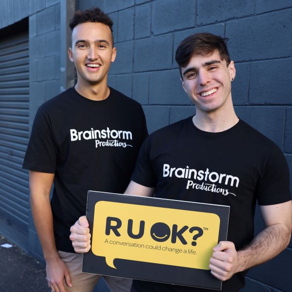 Two actors wearing Brainstorm Productions shirts and holding a sign that says "R U OK? A conversation could change a life"