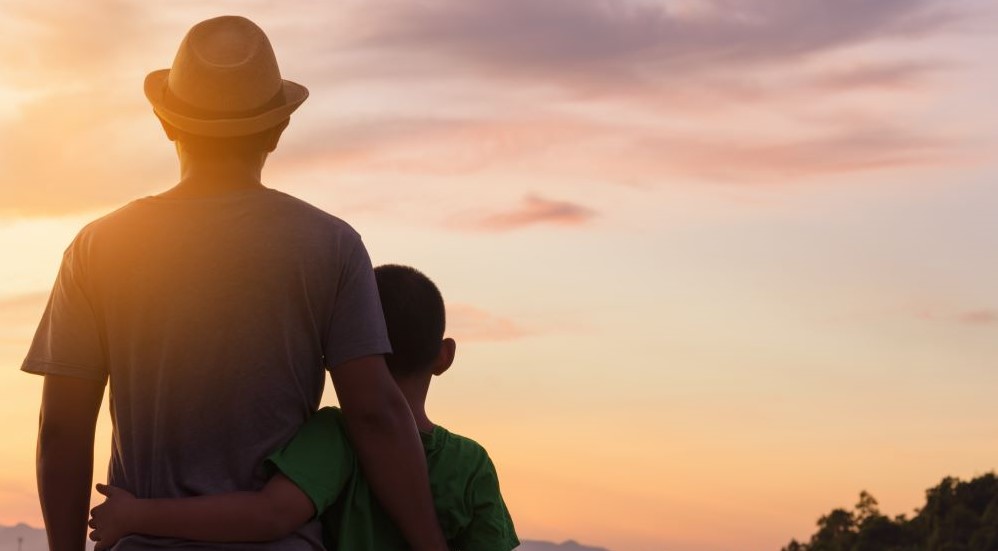 A father and a child looking at a sunset together.