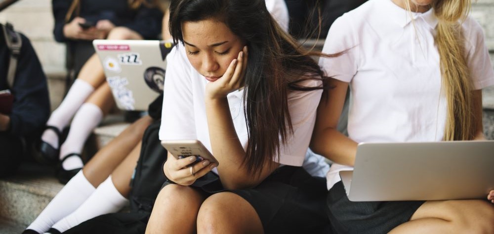 A high school student is sitting on a step looking at her phone and seems concerned.