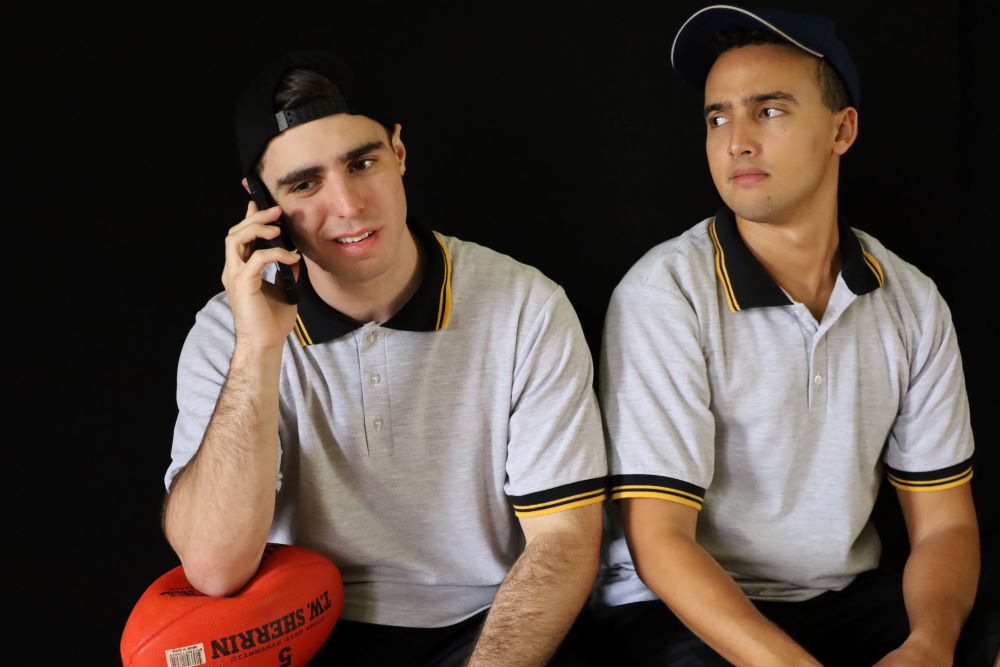 Two actors sitting beside each other, one is on the phone and the other is looking at him with a concerned expression