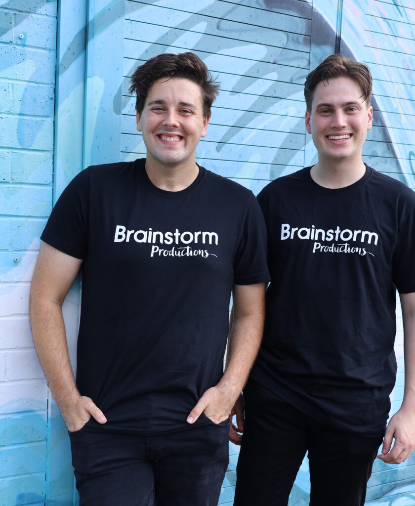 Two Brainstorm actors in company shirts standing in front of a colourful mural