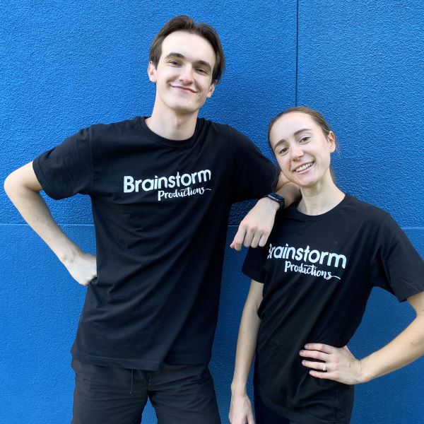 Two actors standing in front of a blue wall wearing Brainstorm t-shirts