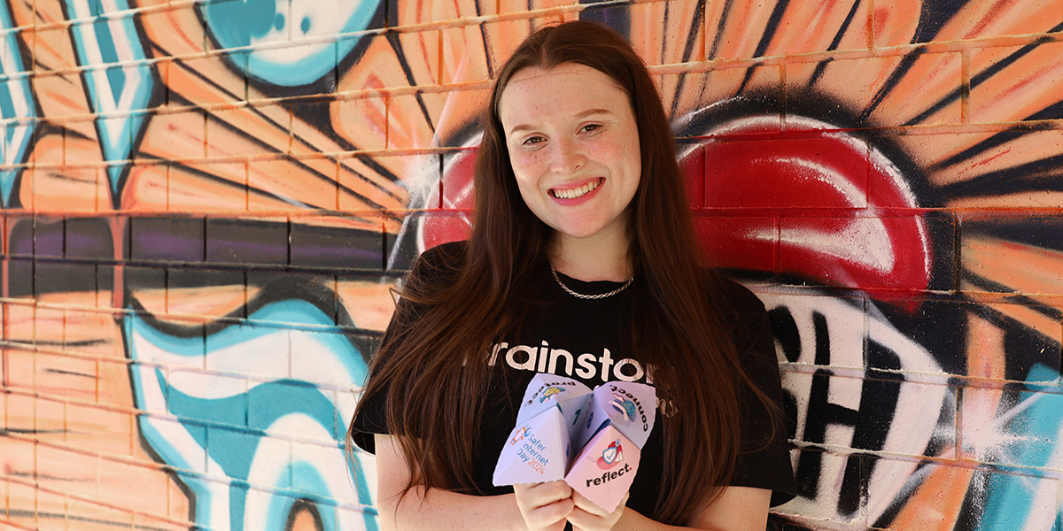 Brainstorm actor Chelsea is standing in front of a brightly painted wall and holding a Safer Internet Day chatterbox