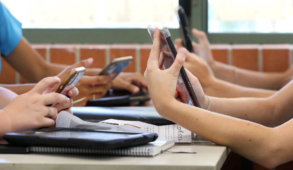 A photo of a group of students in a classroom on their phones and tablets.