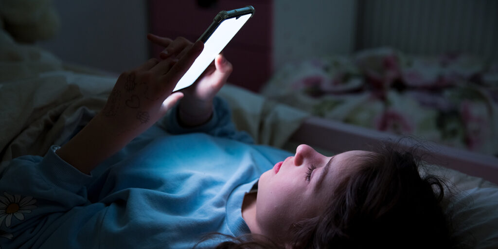 Photo of a young girl looking at her phone in the dark