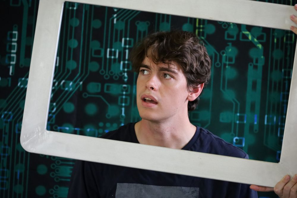 A still from a performance of Cyberia, a bullying prevention and mental health program for high schools. The actor's face is inside a silver frame to look like a device screen.
