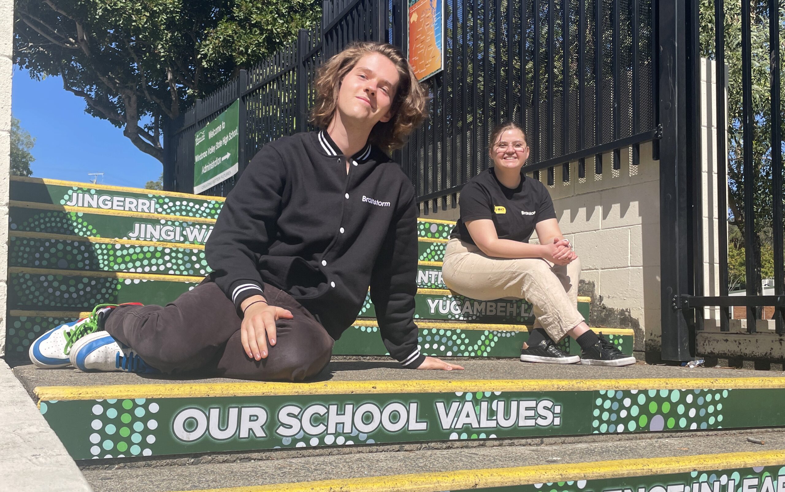 Two Brainstorm actors sitting on some steps and smiling at a school in QLD