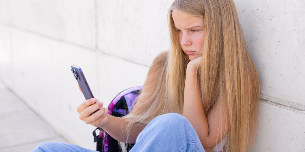 A young teenage girl is looking at her phone with a concerned expression