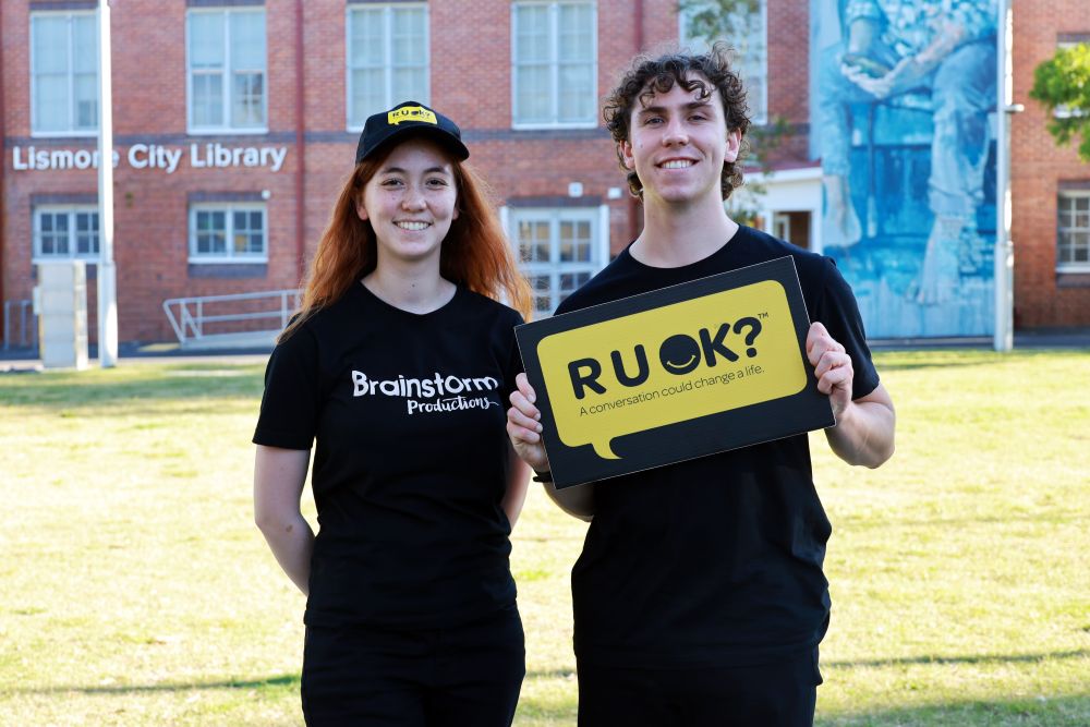 Two Brainstorm actors holding an R U OK sign to show support for R U OK? and R U OK?Day 2026
