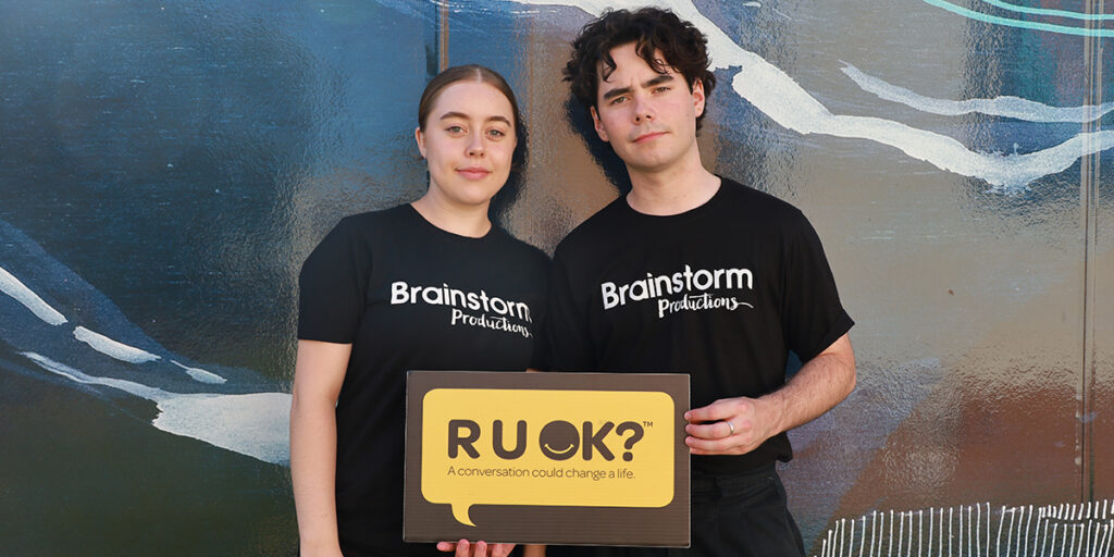 Two Brainstorm actors are holding an R U OK sign to promote mental health awareness and peer support in schools on R U OK?Day 2026